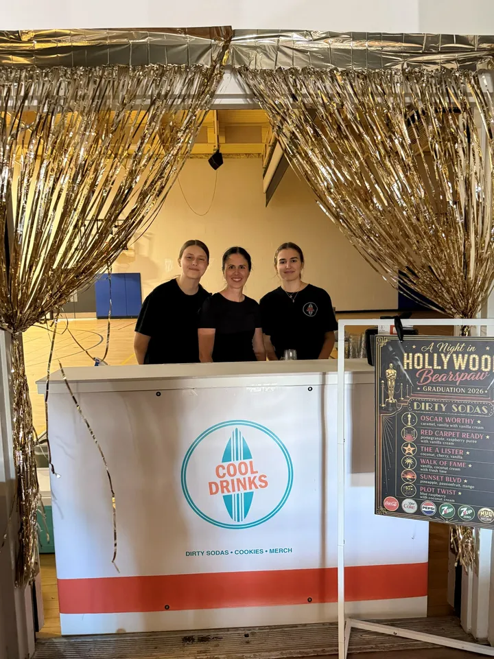Three team members at a Cool Drinks booth dressed up with gold tinsel curtains for a Hollywood-themed event