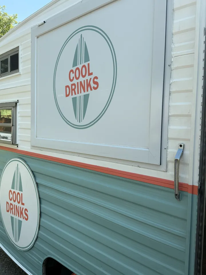 A close-up of the Cool Drinks surfboard logo on the side of the vintage trailer