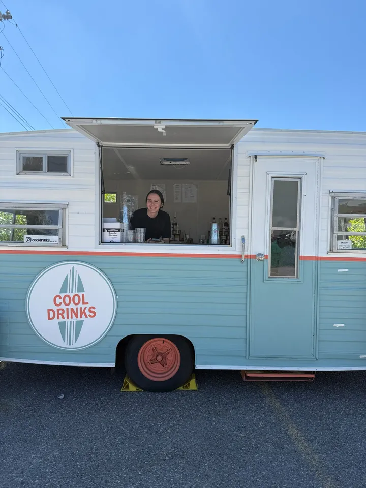 The Cool Drinks vintage trailer with a team member smiling from its serving window